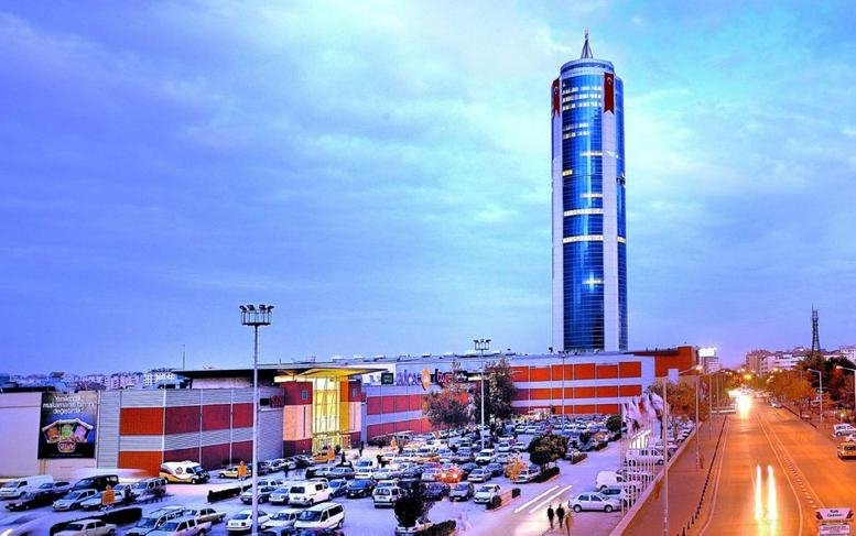 Night view of a tall glass tower illuminated by blue lights above a large parking lot.