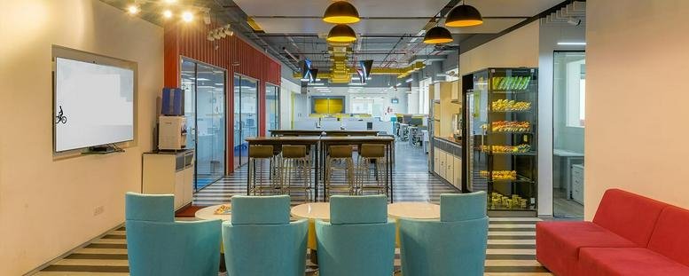 Spacious open-plan communal area with colorful blue and red seating options and a glass-walled corridor.