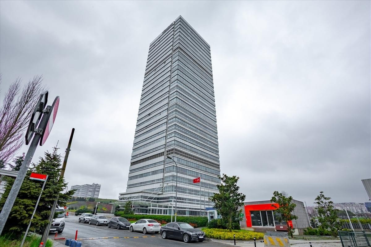 Exterior view of the soaring glass-facade skyscraper Nidakule Göztepe against a grey sky.