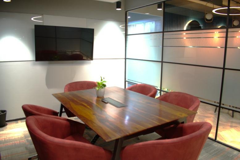 Meeting room at North East Business Center, Ground Floor, Banjara Hills with a wood table and red chairs.