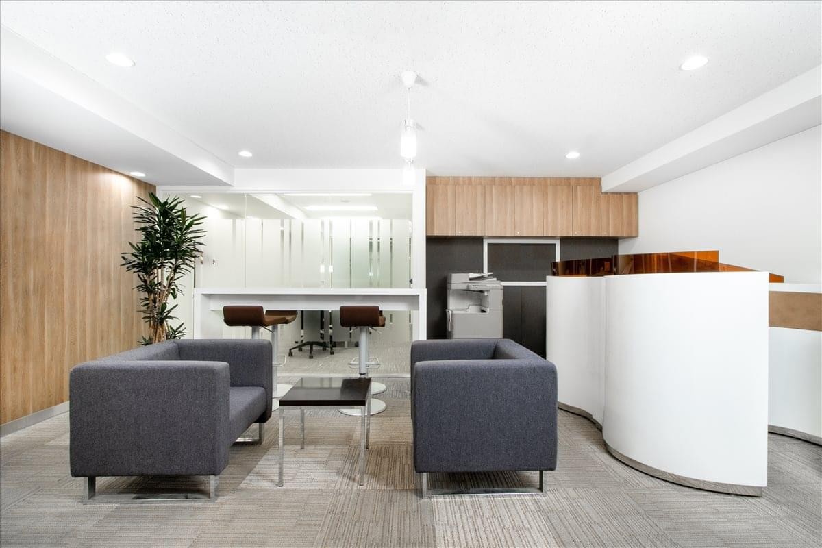 Communal lounge area with grey sofas, a small coffee table, and greenery.