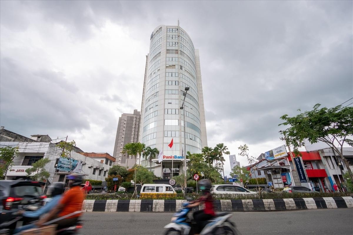 Exterior view of the glass-facade Panin Tower in Balikpapan under a cloudy sky.