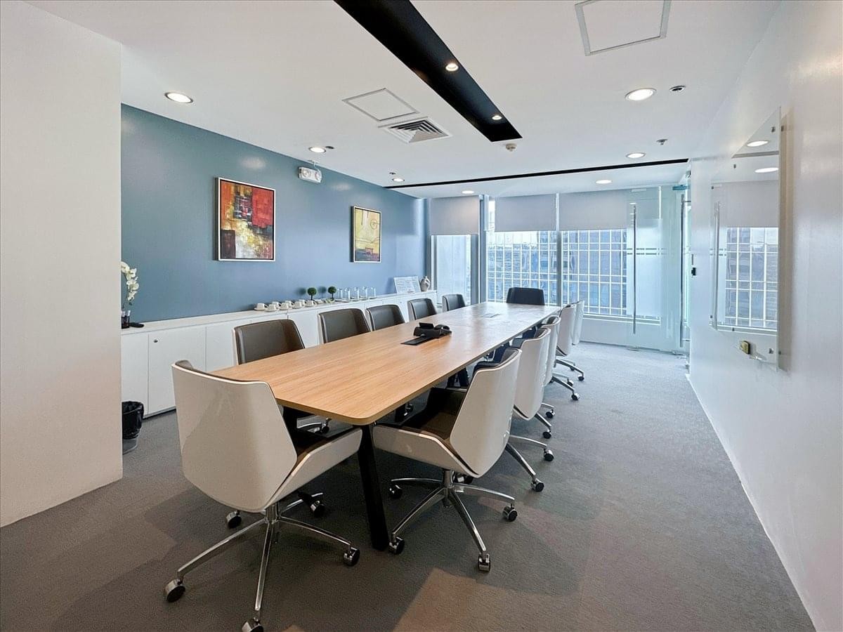 Modern conference room with a large wooden table, white executive chairs, and a blue accent wall with artwork.