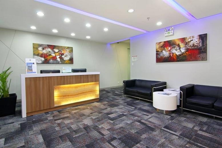 Professional reception desk with warm wooden panels and comfortable black leather sofas.