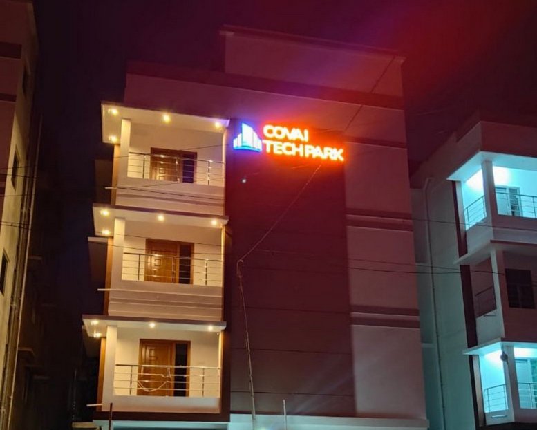 Exterior view of the multi-story Covai Tech Park building at night with glowing orange and blue signage.