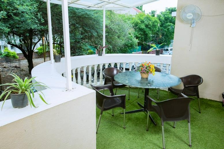Exterior balcony at Plot No. 26 Cosmos Gardens with a round table, chairs, and artificial turf.