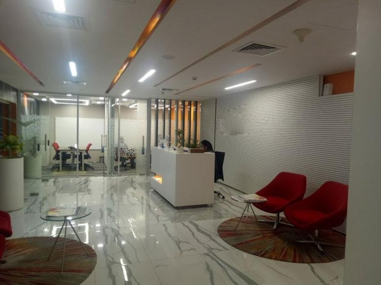 Reception area at Prestige Polygon, Anna Salai with white desk, marble floors and red accent lounge chairs.