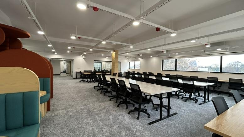 Spacious open-plan coworking area with long white desks and teal booth seating.