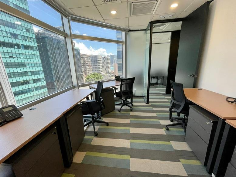 Bright office room with desks, city views through large windows, and striped carpeting.