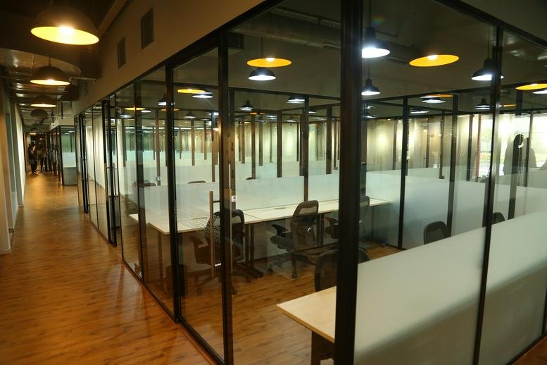 Shared office area with glass partitions and wooden flooring at RMZ Ecoworld, Building 6A.