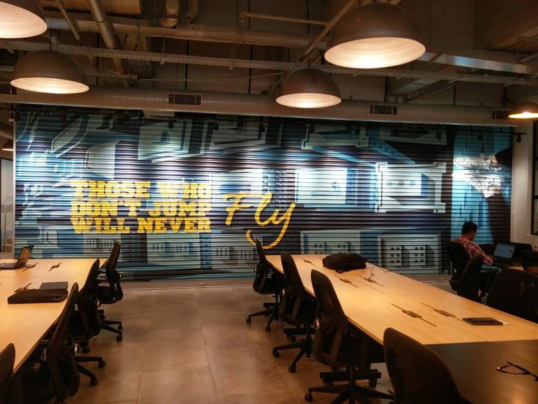 Wide interior view of RMZ Ecoworld, Building 6A featuring long timber desks and an inspirational wall mural.