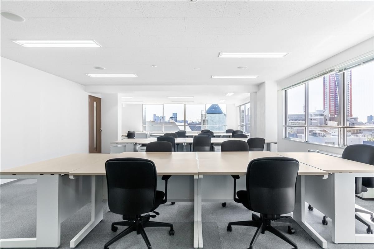Collaborative workspace featuring long rows of desks with city views through large windows.