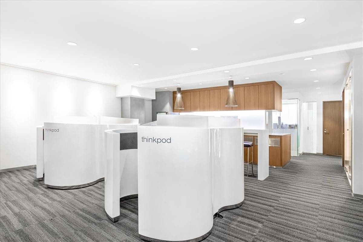 Modern coworking space with unique curved white privacy pods and a kitchen area in the background.