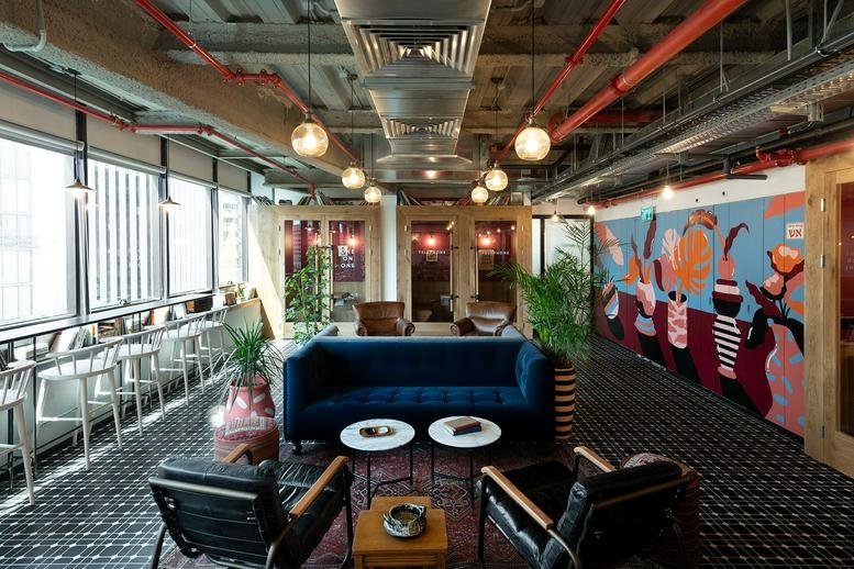 Spacious communal lounge at Rothschild Boulevard 45 featuring a blue velvet sofa and industrial ceilings.