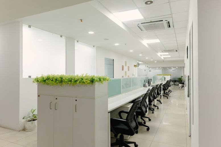 Bright open-plan workspace at RV Tower with white desks, black chairs, and green plant dividers.