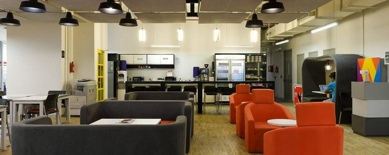 Spacious lounge and breakout area at Samrah Plaza with orange armchairs and a modern kitchen background.