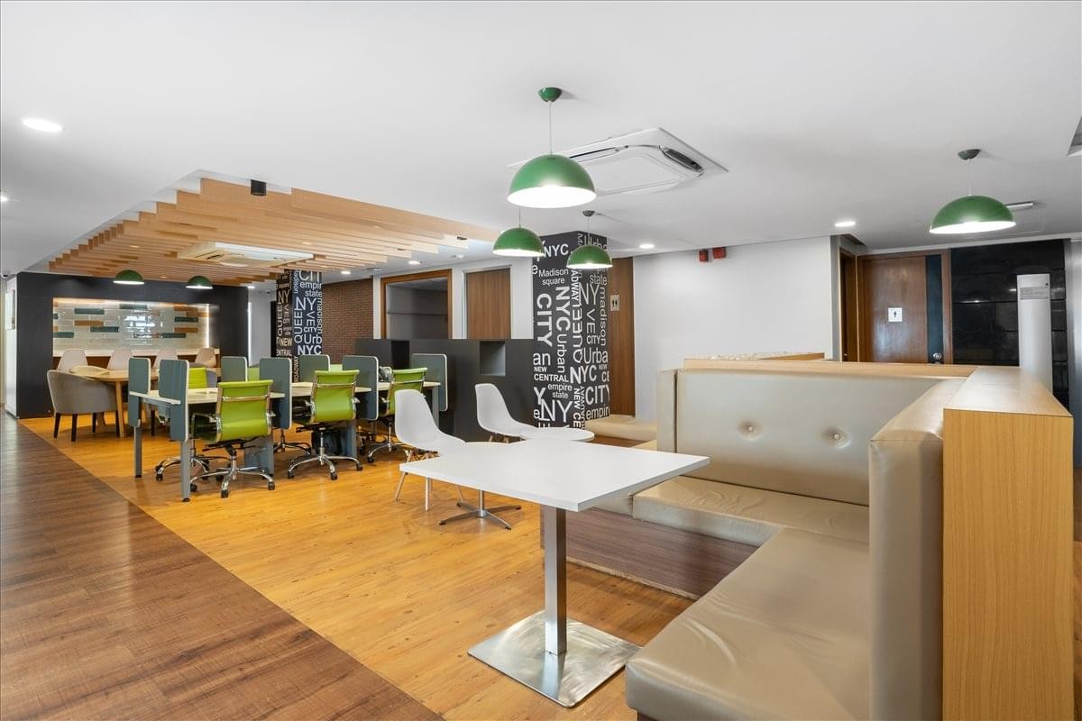 Spacious coworking area with green chairs, wooden floors, and comfortable booth seating.