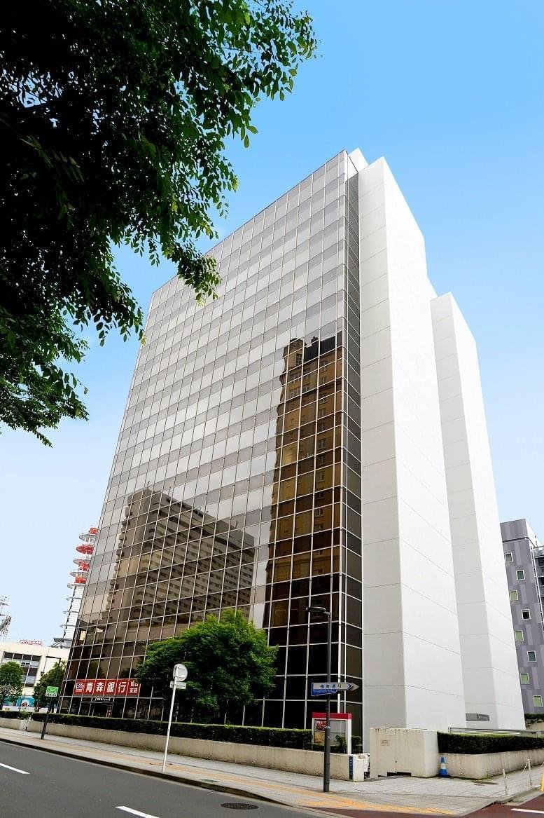 Exterior view of the glass-facade Sendai Capital Tower Building against a blue sky.