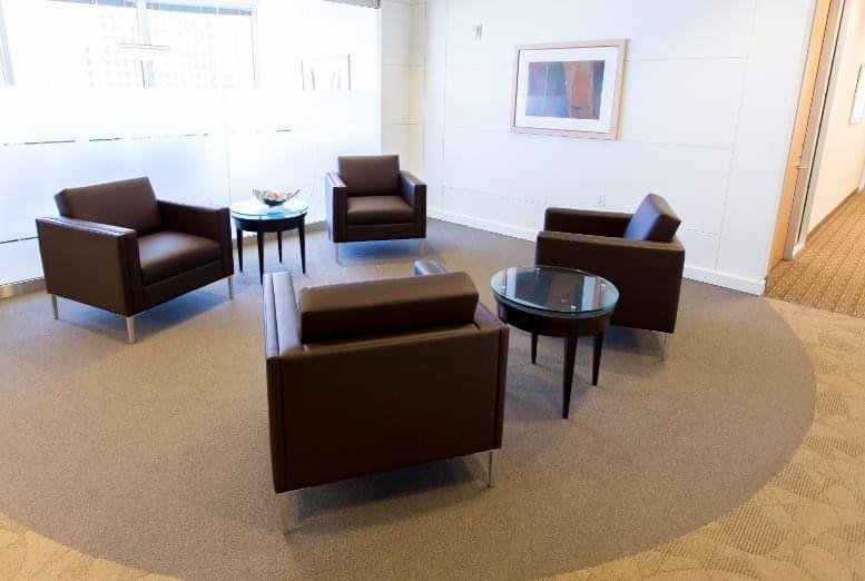 Modern lounge area with four brown leather armchairs and circular coffee tables on a round rug.