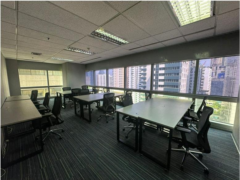 Open-plan workspace with multiple desks and floor-to-ceiling windows showing city views.