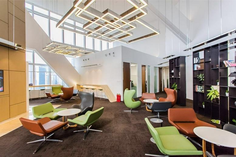 Bright open-plan office lounge with colorful seating and architectural geometric light installations.