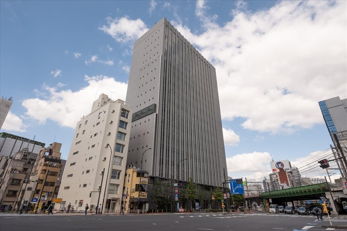 Exterior view of the tall, grey facade of Shinbashi Tokyu Bldg under a blue sky.