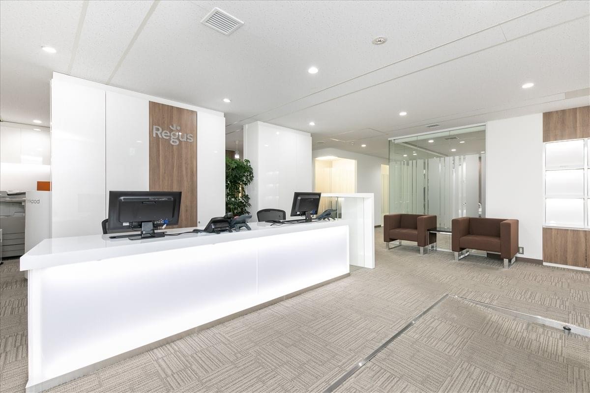 Modern white reception desk with wood panel accents and a waiting area with brown armchairs.