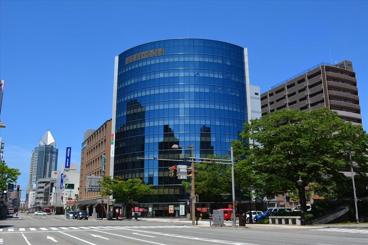 Exterior view of the curved glass-facade 7F Stork Building Kagamibashi under a clear blue sky.
