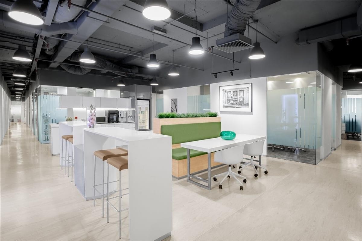 Modern coworking area with high-top tables, a green bench seat, and exposed ceilings.