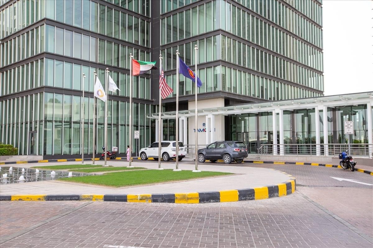 Exterior view of the glass-facade Tamouh Tower showing the entrance and flags.