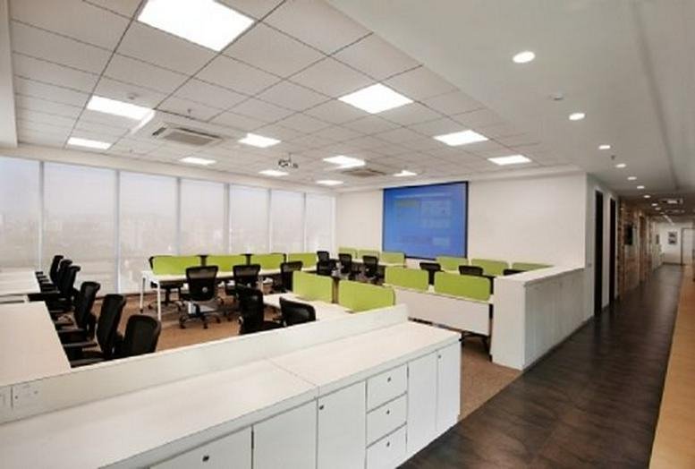Bright open-plan workspace with white desks, green privacy screens, and dark wood flooring.