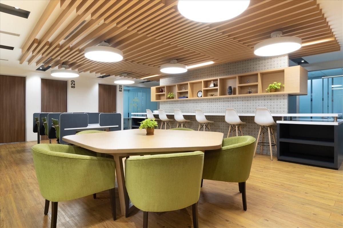 Spacious communal lounge featuring a hexagonal wooden table, green armchairs, and timber ceiling slats.
