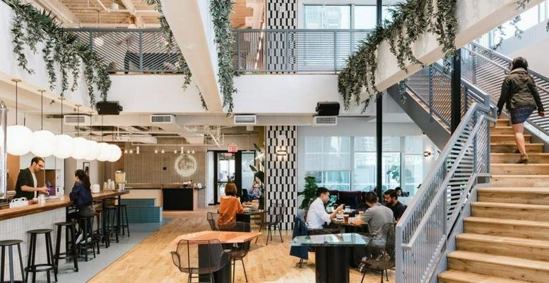 Spacious two-story coworking hub with a staircase, cafe bar, and hanging greenery.
