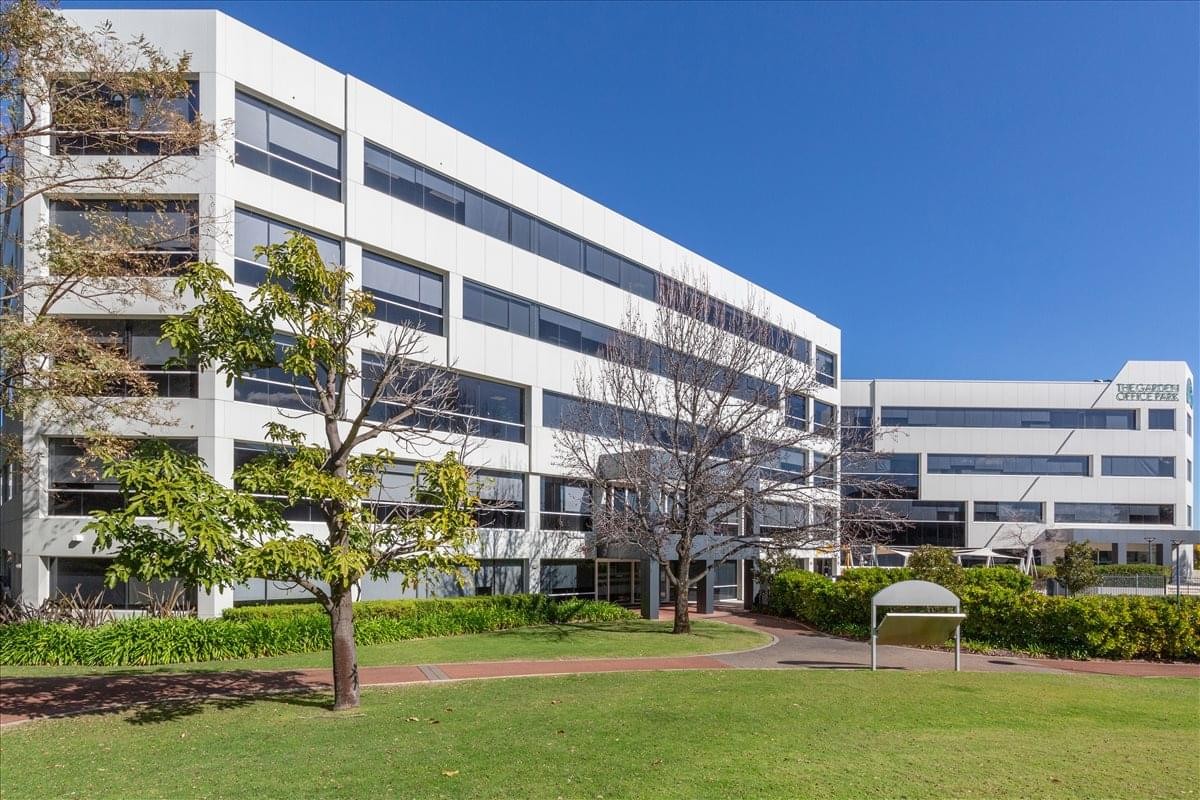 Sunny exterior view of the multi-story Garden Office Park building with green lawn and mature trees.