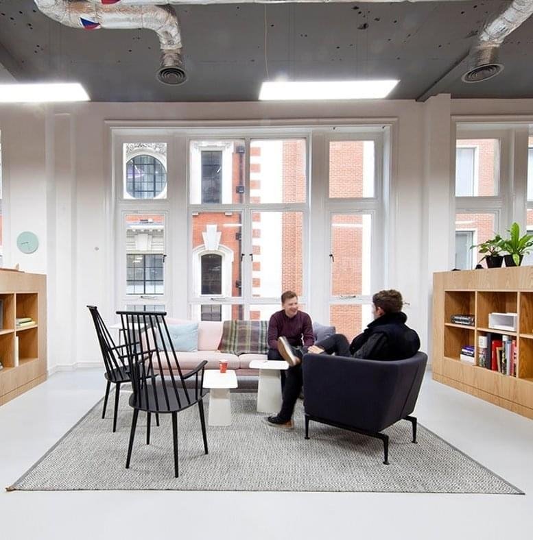 Spacious breakout lounge with a grey rug, designer chairs, and a view of The Lee Gardens 3 facade.
