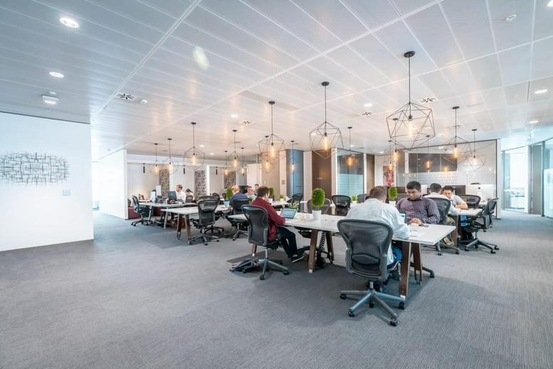 Expansive open-plan coworking area with high ceilings, industrial pendant lights and many desks.