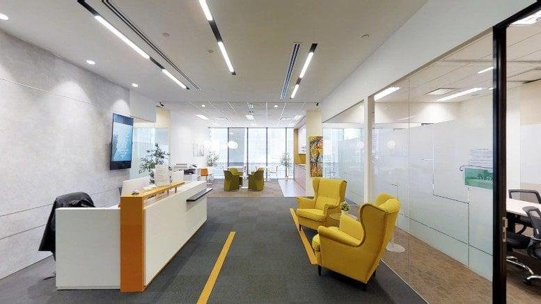 Modern reception desk at Tokio Marine Centre with bright linear lighting and yellow armchairs.