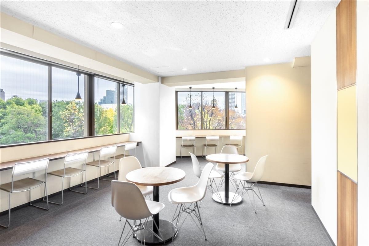 Bright communal lounge with round cafe tables, white chairs, and window seating.
