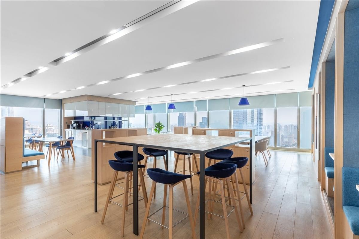 Modern coworking lounge with a high wooden table, navy blue bar stools, and warm wood flooring.