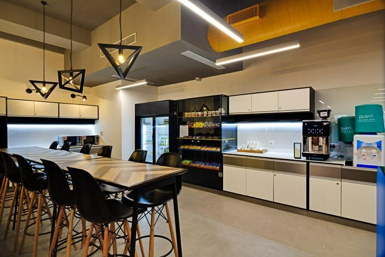 Spacious communal breakroom at Business@Mantri featuring a kitchenette, coffee station, and high-top seating.