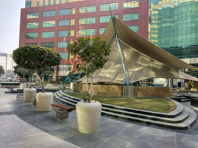 Modern exterior courtyard at Unitech Cyberpark, Sector 39, Gurgaon featuring tiered seating and a canopy.