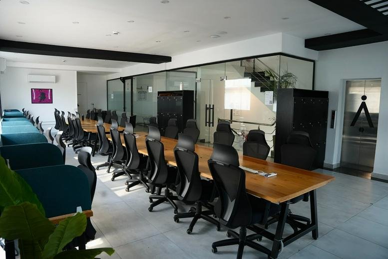 Spacious open-plan workspace at Uthman Ibn Affan Road with long wooden desks and ergonomic black chairs.