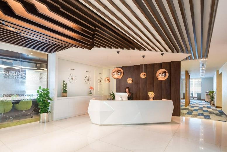 Reception area at Vision Tower, Business Bay featuring a geometric desk and slatted wood ceiling.