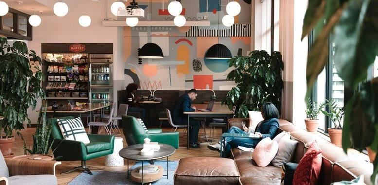Spacious communal lounge featuring green velvet armchairs, leather sofas, and vibrant wall art.