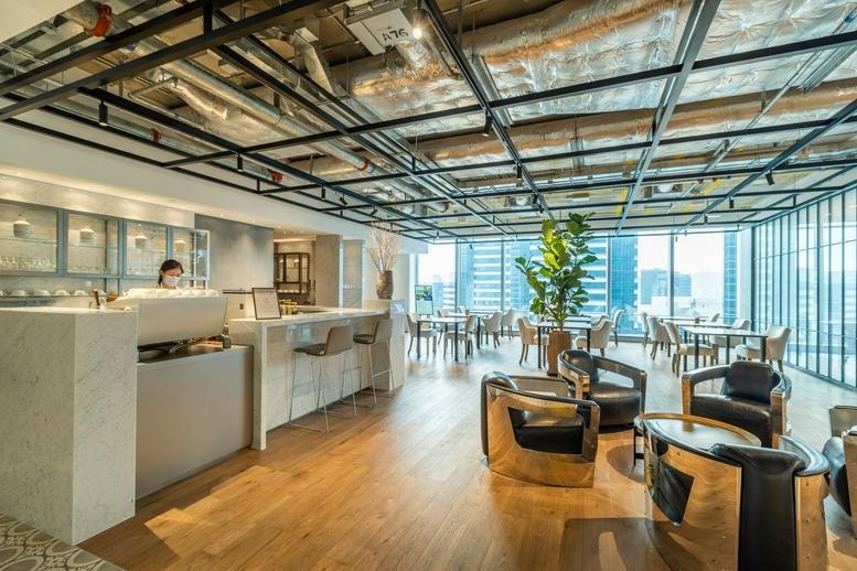 Spacious lounge at One Island East, Level 23 & 60 featuring a cafe bar, warm wood floors, and floor-to-ceiling windows.