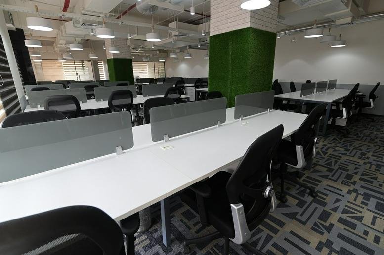 Open-plan workspace at Infra Futura featuring long white desks and pillars covered in green turf.