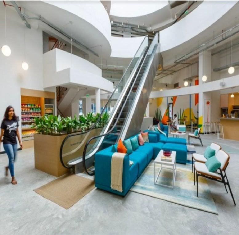Lobby and lounge at Panchshil Futura with a grand escalator, teal sectional sofa, and skylight atrium.
