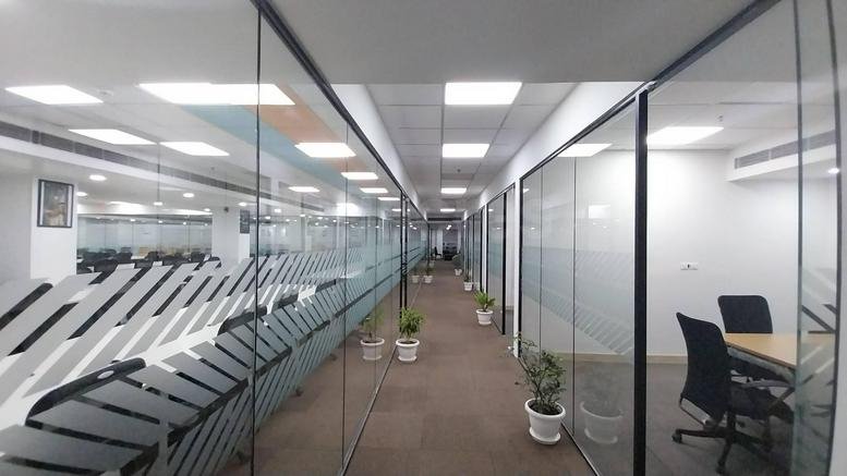 Bright hallway at Acquir Brickworks, Plot 31A, Udyog Vihar Phase 4 with glass-walled offices and potted plants.