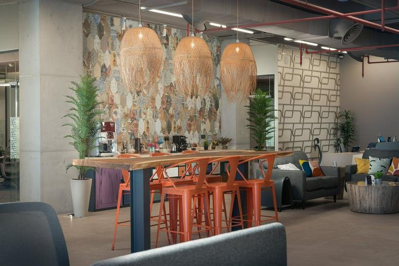 Communal break area at Sumou Tower featuring woven pendant lights, orange stools, and a patterned feature wall.
