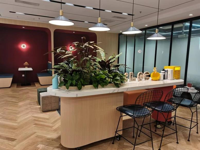 Warm communal break area at Qingdao International News Center with a marble-top island, plants, and stylish bar stools.